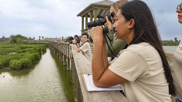 Children on a wooden bridge trail with the person in the foreground using binoculars.