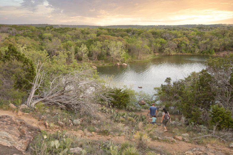To people walking a trail towards a lake.