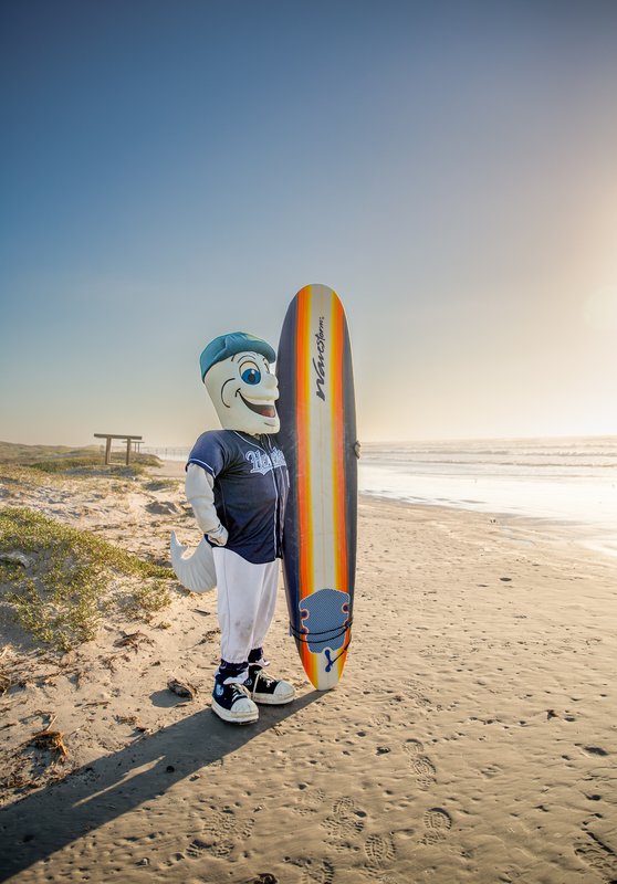 Corpus Christi Hooks mascot Rusty on the beach at Mustang Island State Park holding a surfboard.