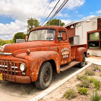 Rusted red vintage truck sitting outside BBQ joint.