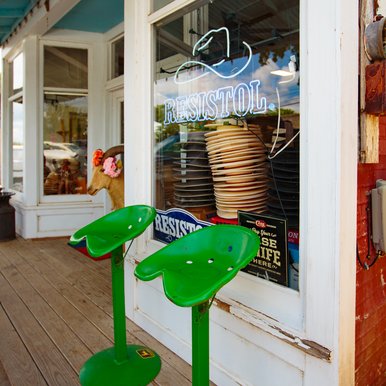 Green tractor style chairs outside a hat shop.