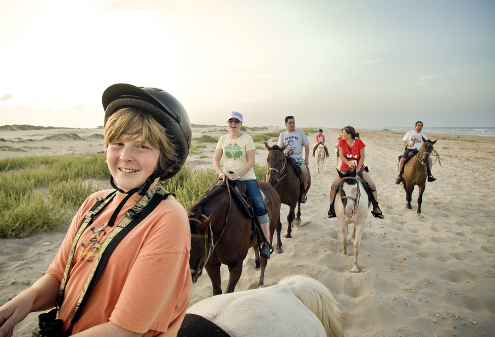 a group of horseback riders trot along the sandy shore of South Padre Island