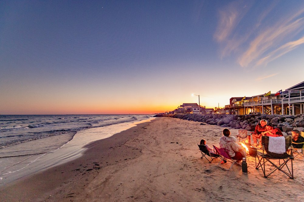A family sits on camp chairs around a fire on the sands of Surfside beach