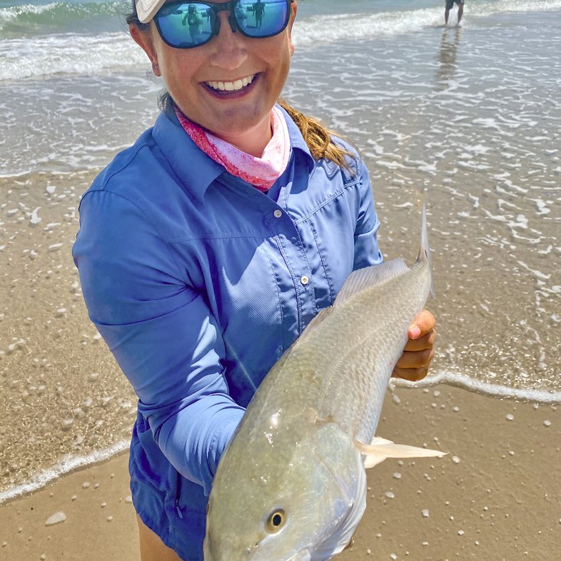 A woman angler stands in the waters of the gulf and shows off her catch