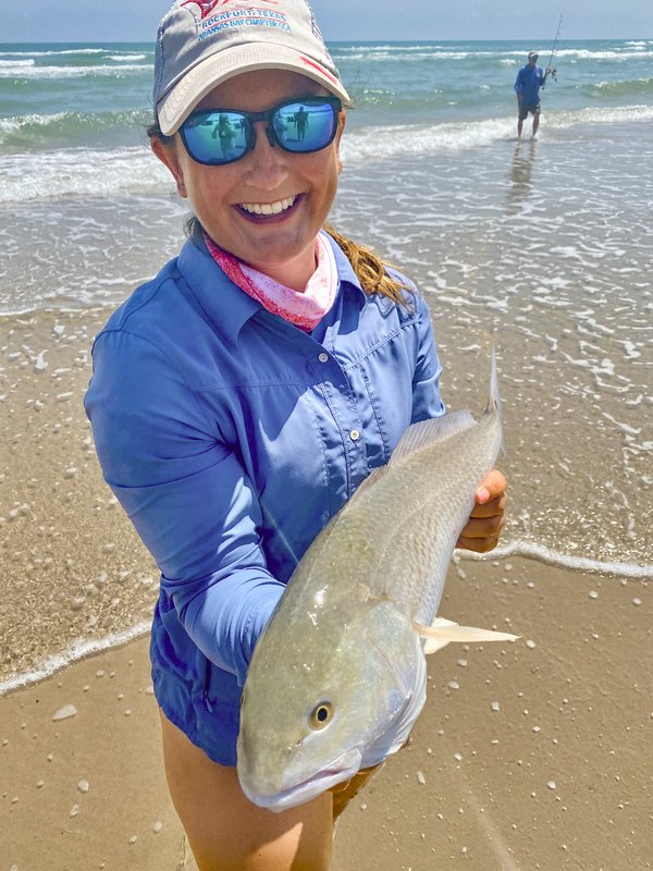 A woman angler stands in the waters of the gulf and shows off her catch