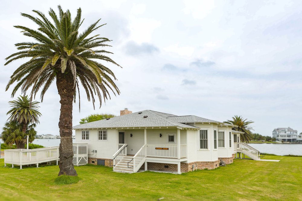 A palm tree grows in front of the white beach lodge at Galveston Island State Park