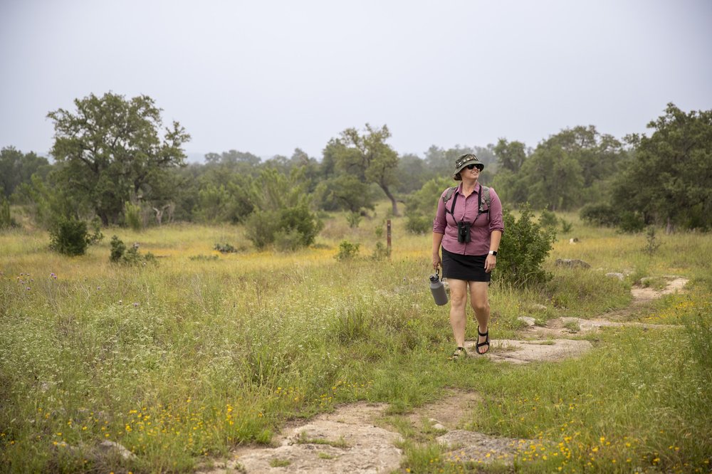 A woman in a pink shirt and a bucket hat walks along the Painted Bunting Trail at Guadalupe River State Park