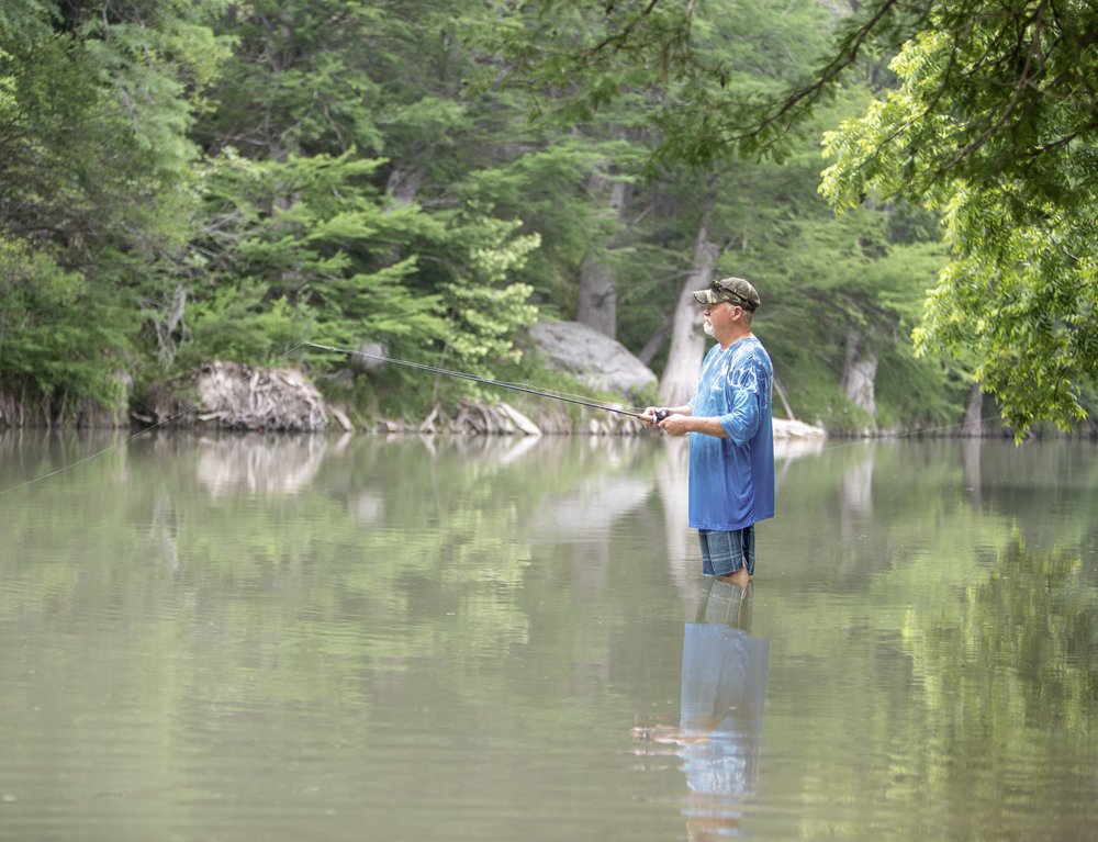 A young man stands in knee-deep water fishing in the Guadalupe River