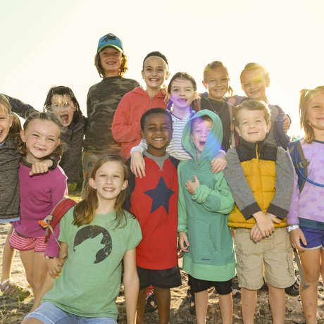 Thirteen young children at a park cluster together posing for a photograph
