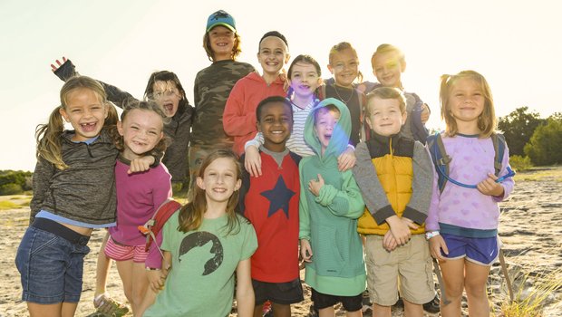 Thirteen young children at a park cluster together posing for a photograph