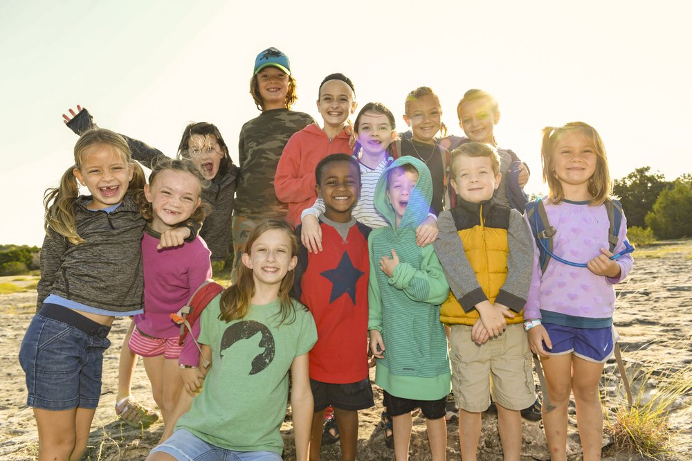 Thirteen young children at a park cluster together posing for a photograph