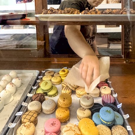 A woman selects a colorful macaron cookie from a tray at Weatherford's Hometown Bakery