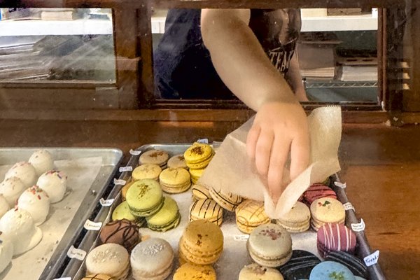 A woman selects a colorful macaron cookie from a tray at Weatherford's Hometown Bakery