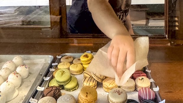 A woman selects a colorful macaron cookie from a tray at Weatherford's Hometown Bakery