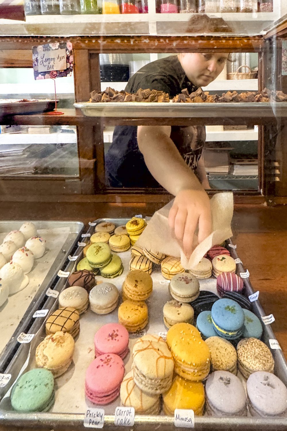 A woman selects a colorful macaron cookie from a tray at Weatherford's Hometown Bakery