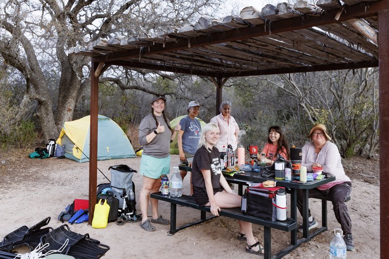 Group of women at Del Norte SNA campsite eating dinner around covered picnic table