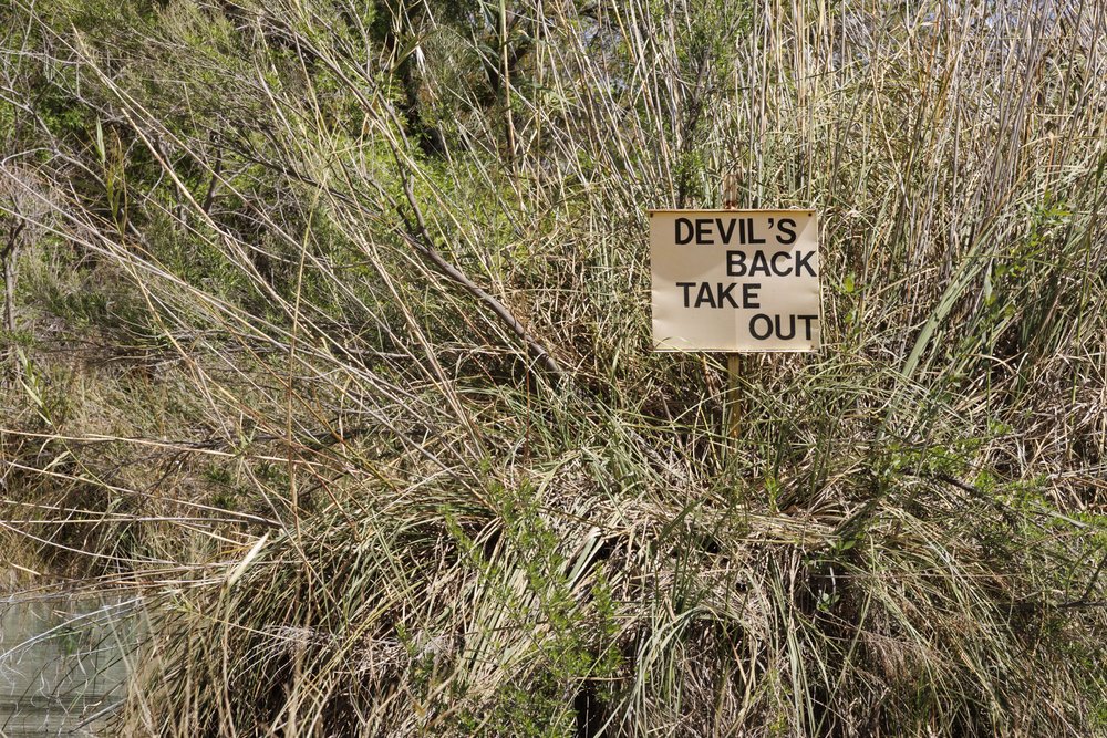 Devil's Back Take Out sign surrounded by weeds on the Devils River
