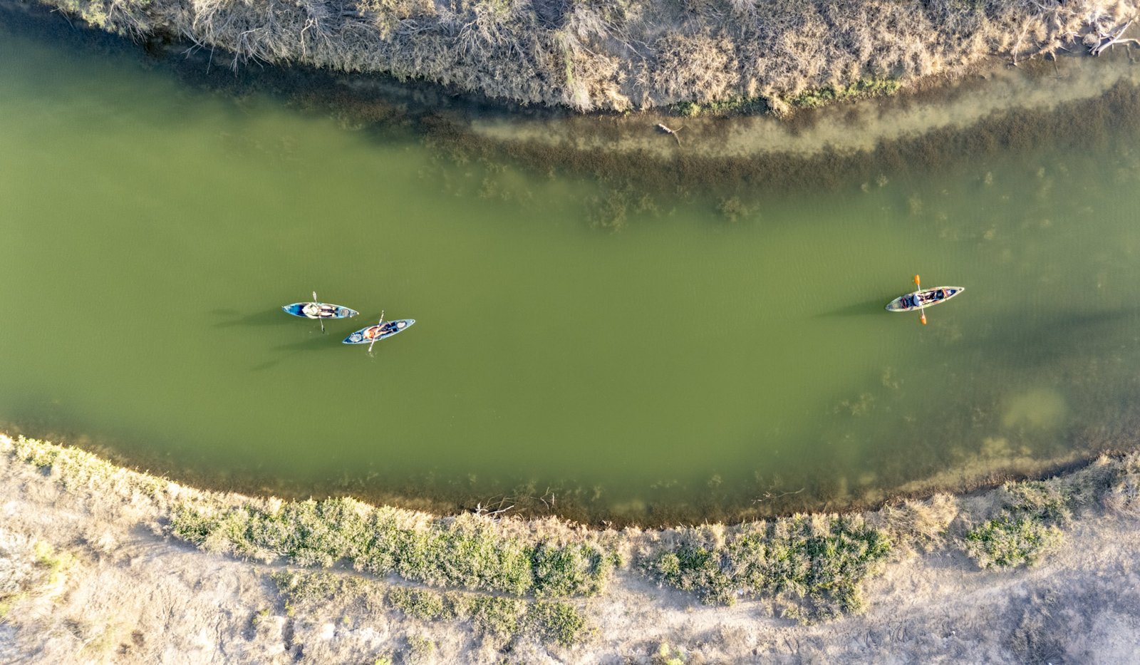 A bird's eye view of two kayakers paddling the green Pecos River