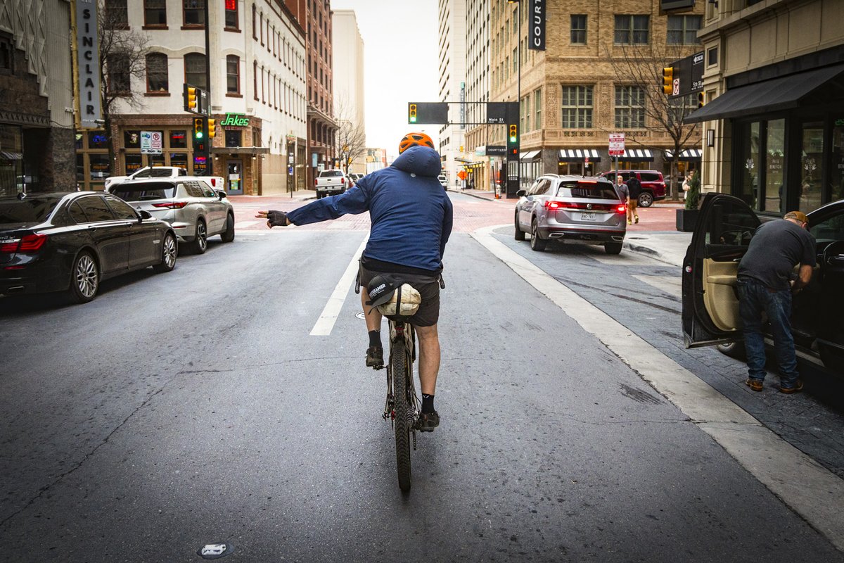 A person riding a bike on city streets signaling a turn.
