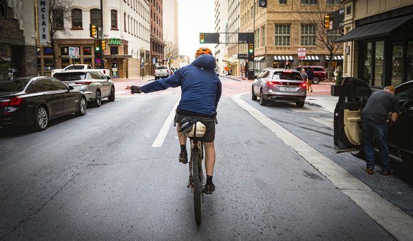 A person riding a bike on city streets signaling a turn.