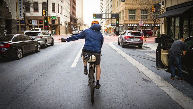 A person riding a bike on city streets signaling a turn.