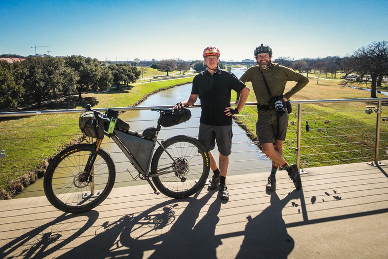 Two people on a trail with a bike stand near a fence.