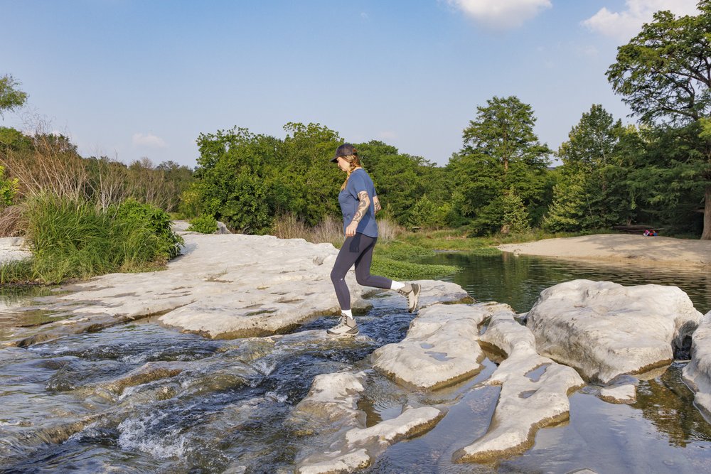 A person jumping rocks in the water on a trail.