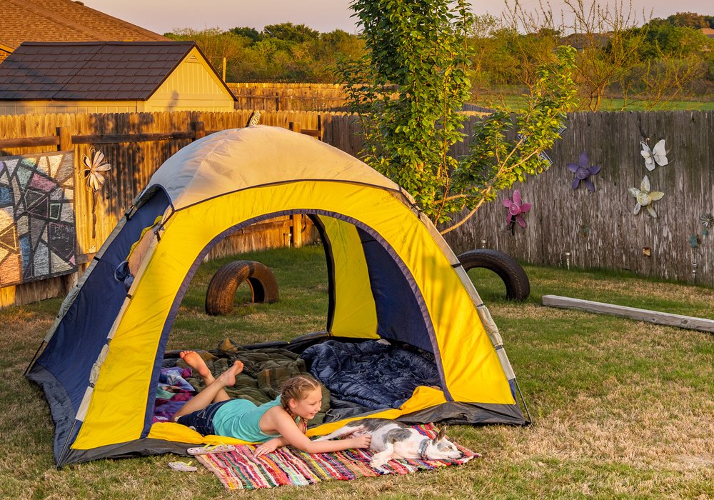a young girl and a dog lay in a tent in a fenced backyard