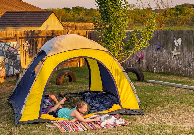 a young girl and a dog lay in a tent in a fenced backyard
