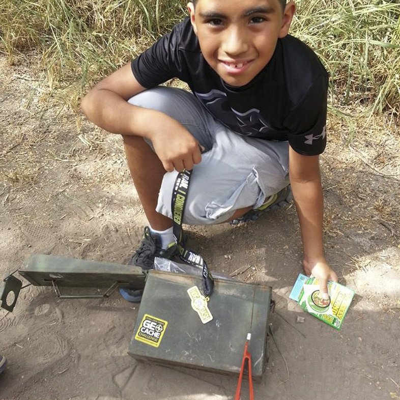 A young boy crouches in front of a geocache at Resaca de la Palma state park