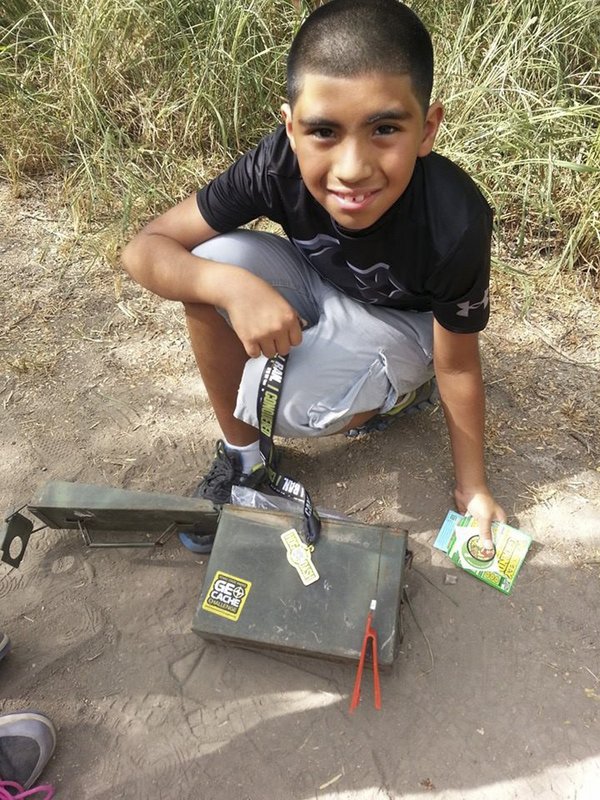 A young boy crouches in front of a geocache at Resaca de la Palma state park