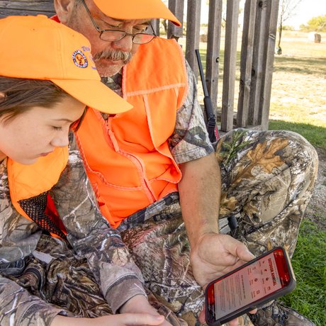 An older hunter shows a younger hunter the Outdoor Annual app on his smartphone