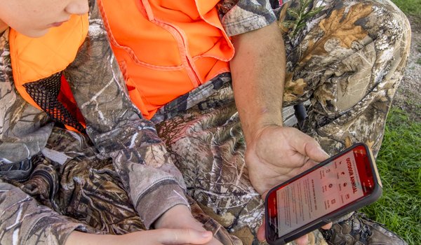 An older hunter shows a younger hunter the Outdoor Annual app on his smartphone