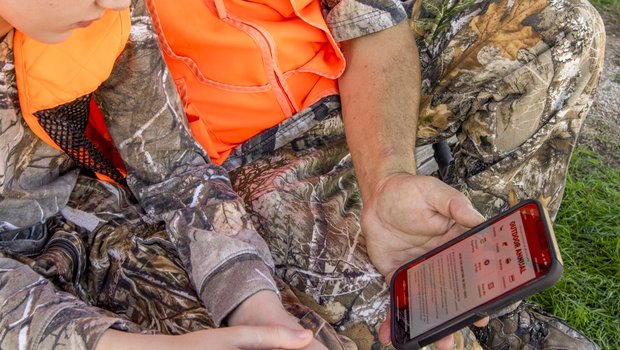 An older hunter shows a younger hunter the Outdoor Annual app on his smartphone