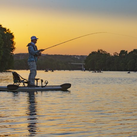 An angler fishes from a kayak as the sun sets