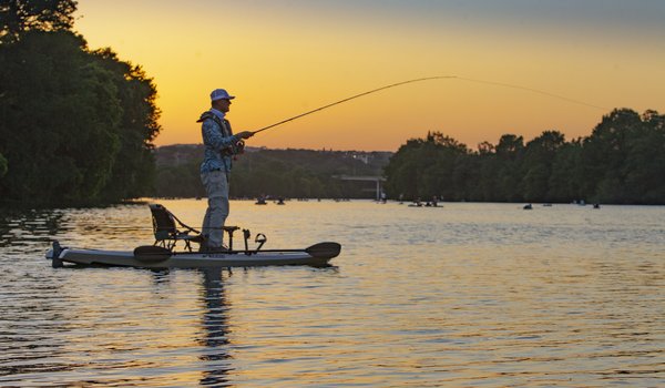 An angler fishes from a kayak as the sun sets