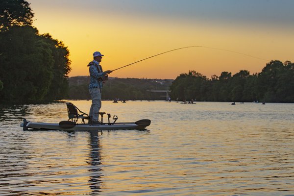 An angler fishes from a kayak as the sun sets
