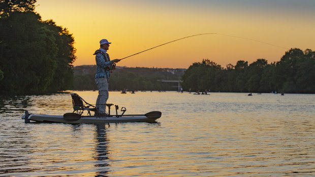 An angler fishes from a kayak as the sun sets