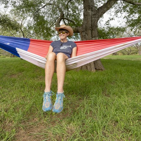Wearing a cowboy hat, sunglasses, t-shirt and shorts, Pam LeBlanc sits inside a hammock designed to look like the Texas state flag