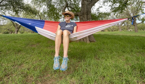 Wearing a cowboy hat, sunglasses, t-shirt and shorts, Pam LeBlanc sits inside a hammock designed to look like the Texas state flag