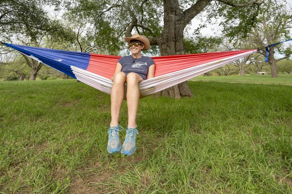 Wearing a cowboy hat, sunglasses, t-shirt and shorts, Pam LeBlanc sits inside a hammock designed to look like the Texas state flag