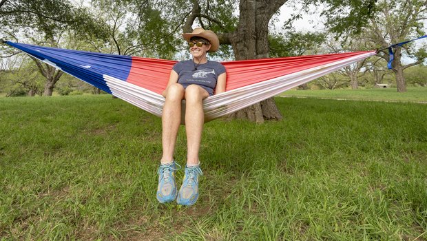 Wearing a cowboy hat, sunglasses, t-shirt and shorts, Pam LeBlanc sits inside a hammock designed to look like the Texas state flag