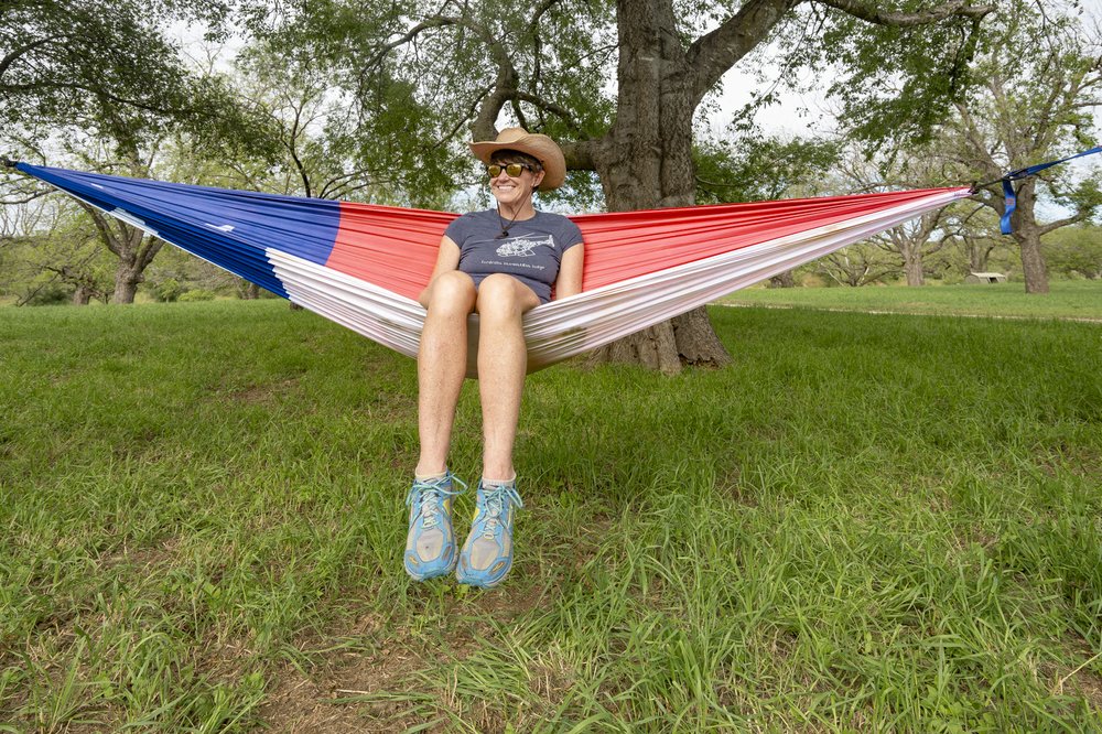 Wearing a cowboy hat, sunglasses, t-shirt and shorts, Pam LeBlanc sits inside a hammock designed to look like the Texas state flag
