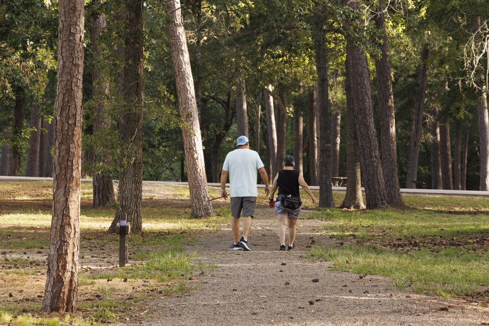 Two hikers walk among the pine trees along the Trinity Trace Trail at Lake Livingston State Park