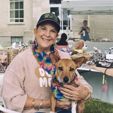 Connie Booth sits in white chair holding her dog on her lap