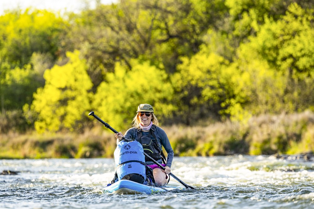 Female paddler kneeling on board while going down some rapids on the Brazos River