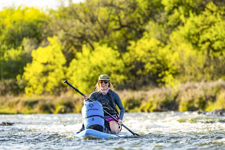 Female paddler kneeling on board while going down some rapids on the Brazos River