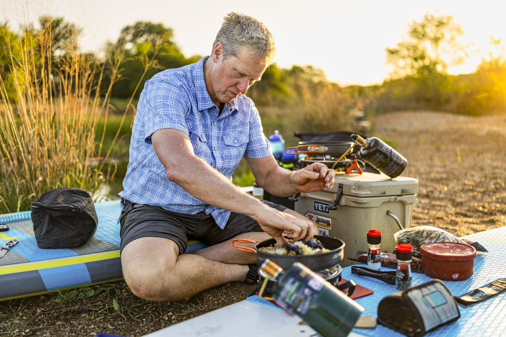 Male camper preparing dinner on a portable cooking device while on the banks of the Brazos River