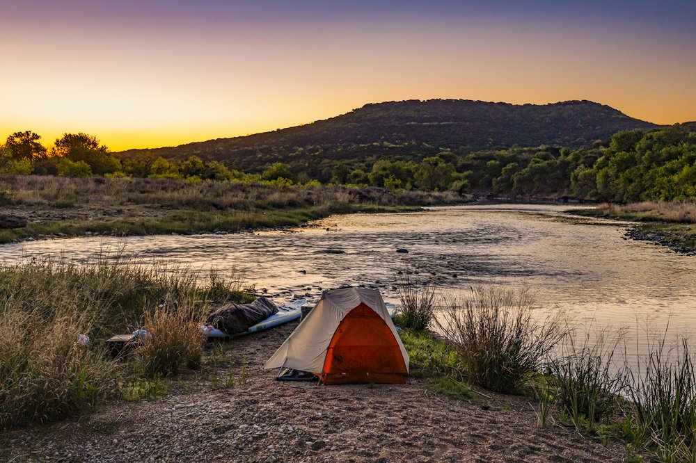 Tent and pair of paddle boards at dusk on the bank of Brazos River