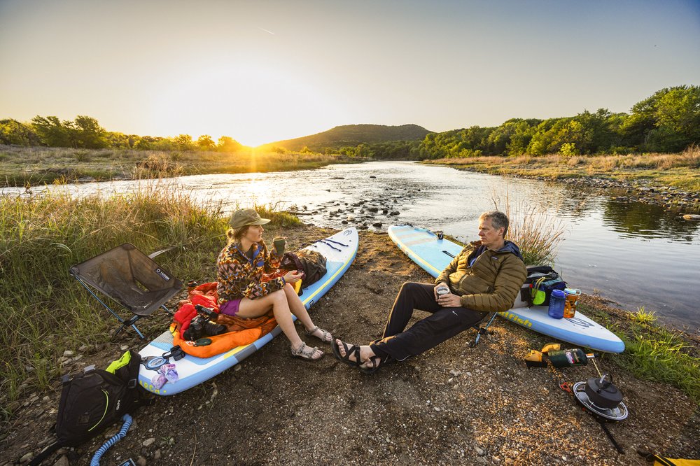 Pair of paddlers resting on their SUP on the banks of Brazos River at sunset